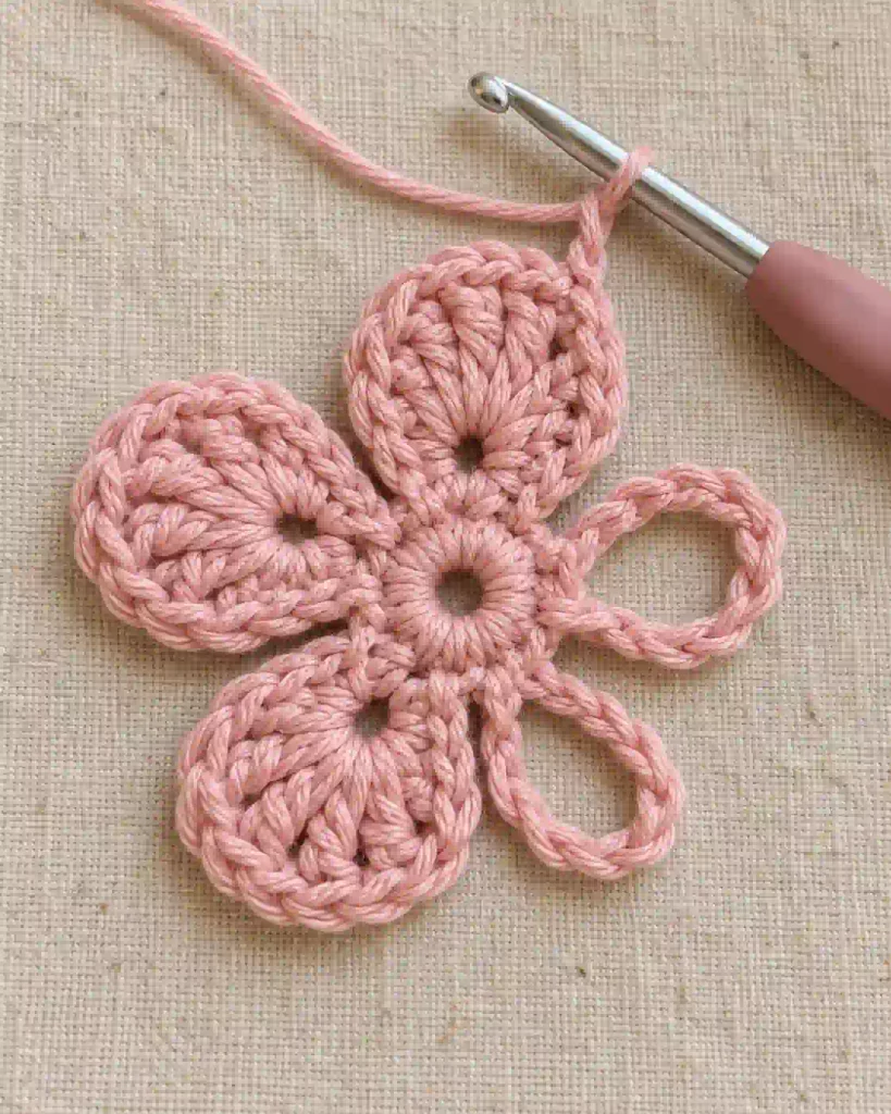 Partially completed five petal crochet flower with three rounded petals and two empty chain loops