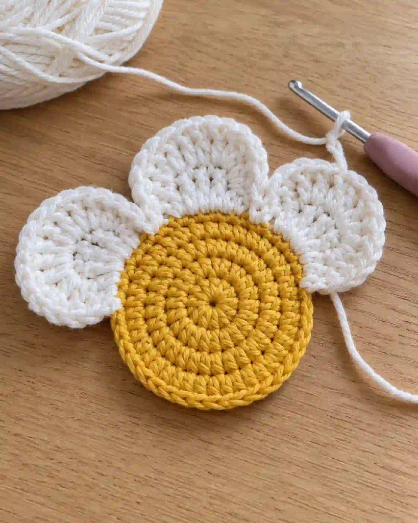 Close-up of white crochet petals attached to a yellow circular coaster center